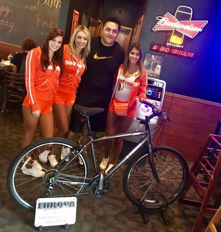 man poses with three women in front of newly won bicycle