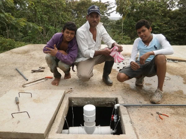 three Nicaraguan men kneel near their new water chlorination system