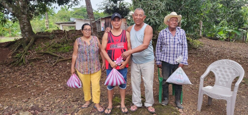 4 people standing by trees holding bags of seed in their hands.